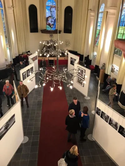 Witte expositiewanden in een kerk met foto's er aan opgehangen.